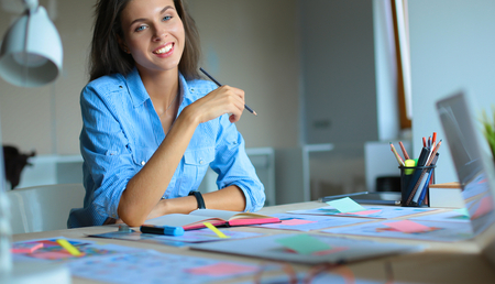 Young woman sitting at the desk with instruments, plan and laptopの写真素材