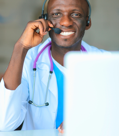 Portrait of young male doctor wearing headset while using computer at desk in clinicの写真素材