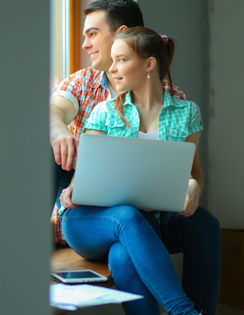 Portrait of young couple moving in new home sitting with laptopの写真素材