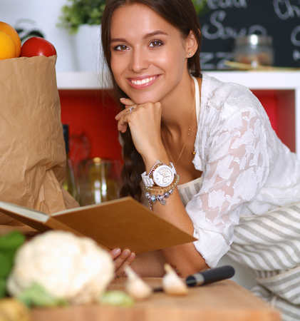 Young woman reading cookbook in the kitchen, looking for recipeの写真素材
