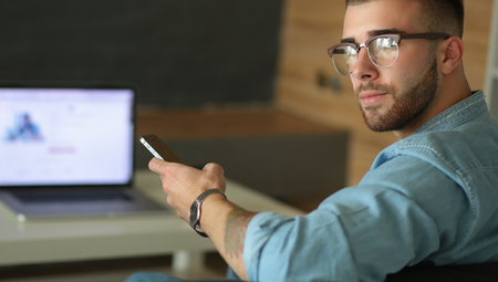 Young man using phone and works on the laptop.の写真素材