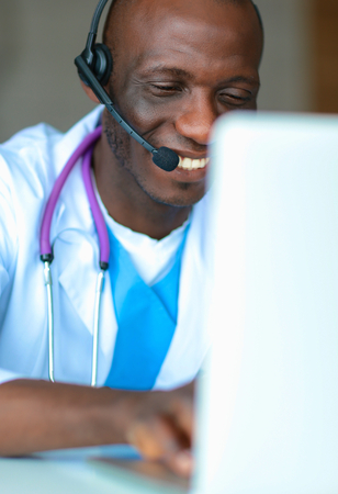 Portrait of young male doctor wearing headset while using computer at desk in clinicの写真素材