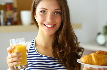 Young woman with glass of juice and cakes standing in kitchen .の写真素材