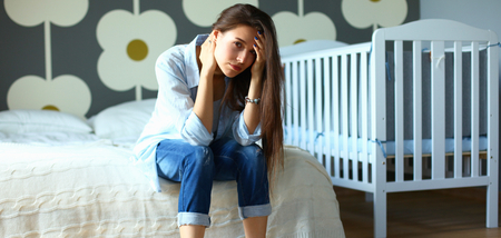 Young tired woman sitting on the bed near childrens cot.の写真素材