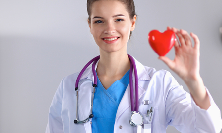 Young woman doctor holding a red heart, standing on grayの写真素材