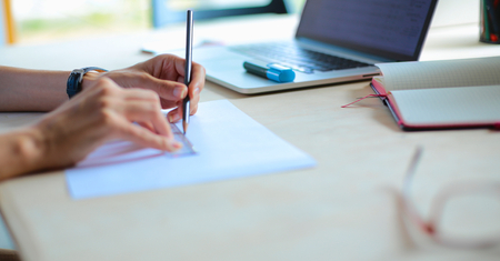 Young woman sitting at the desk with instruments, plan and laptopの写真素材