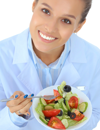 Portrait of a beautiful woman doctor holding a plate with fresh vegetablesの写真素材