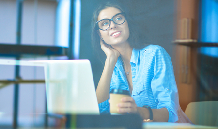 Young woman sitting at office table with laptop,view through windowの写真素材