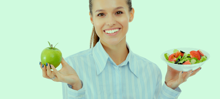 Portrait of a beautiful woman doctor holding a plate with fresh vegetables and green appleの写真素材