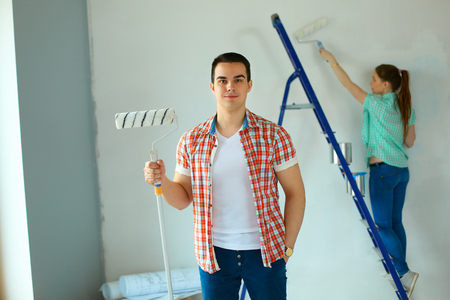 Portrait of happy smiling young couple painting interior wall new house.の写真素材