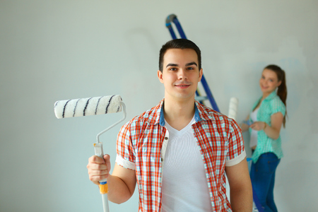 Portrait of happy smiling young couple painting interior wall new house.の写真素材