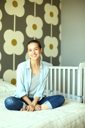 Young woman sitting on the bed near childrens cot.の写真素材