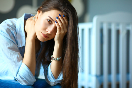 Young tired woman sitting on the bed near childrens cot.の写真素材