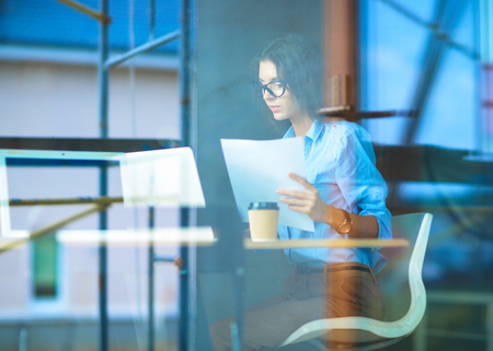 Young woman sitting at office table with laptop,view through windowの写真素材