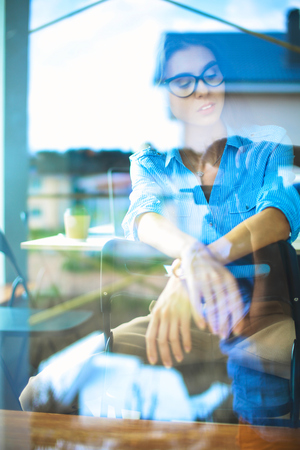 Young woman sitting at office table with laptop,view through windowの写真素材