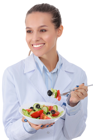Portrait of a beautiful woman doctor holding a plate with fresh vegetablesの写真素材