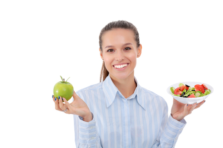 Portrait of a beautiful woman doctor holding a plate with fresh vegetables and green appleの写真素材