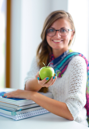 Female college students sitting on the desk with apple a pile of books.の写真素材