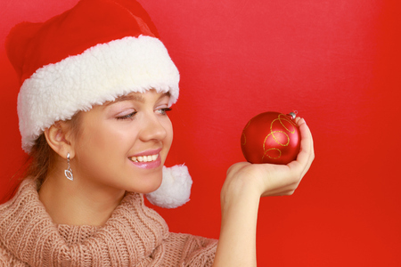 Pretty brunette woman in shirt and santas hat holding red christmas ball.の写真素材