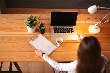 Portrait of relaxed young woman sitting at her desk holding cup of coffeeの写真素材