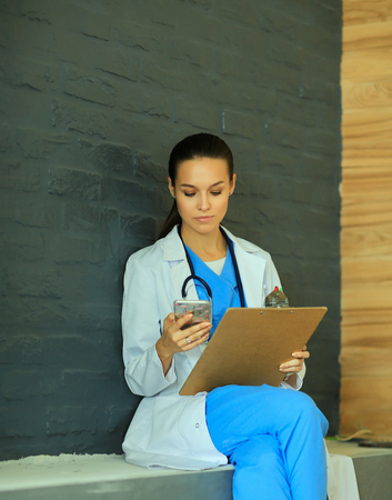 Young woman doctor sitting with your phone.の写真素材