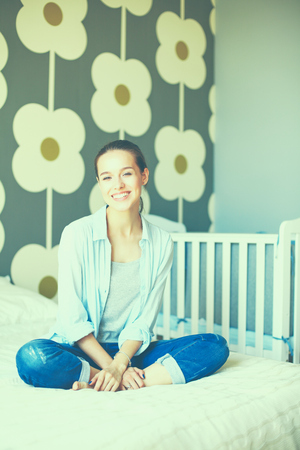Young woman sitting on the bed near childrens cot.の写真素材