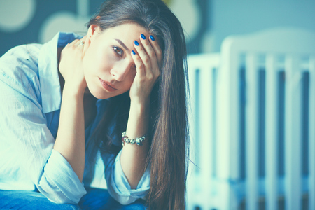 Young tired woman sitting on the bed near childrens cot.の写真素材