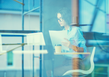 Young woman sitting at office table with laptop,view through windowの写真素材