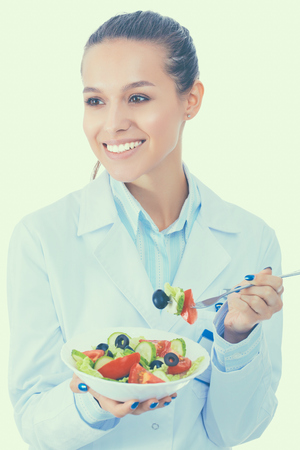 Portrait of a beautiful woman doctor holding a plate with fresh vegetablesの写真素材