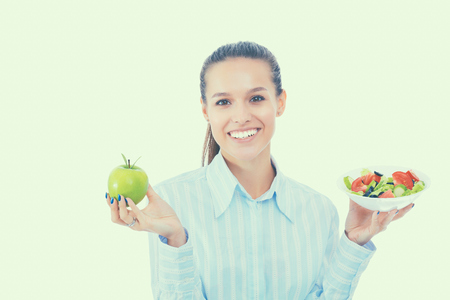 Portrait of a beautiful woman doctor holding a plate with fresh vegetables and green appleの写真素材