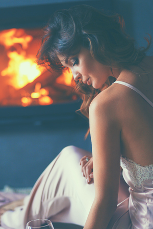 Woman with a glass of wine by the fireplace.の写真素材