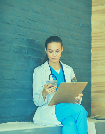 Young woman doctor sitting with your phone.の写真素材