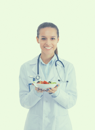 Portrait of a beautiful woman doctor holding a plate with fresh vegetablesの写真素材