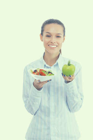 Portrait of a beautiful woman doctor holding a plate with fresh vegetables and green appleの写真素材
