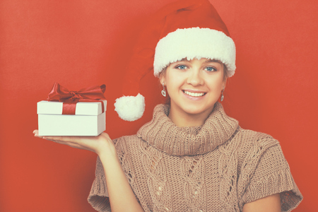 Santa girl holding Christmas gift on red background.の写真素材