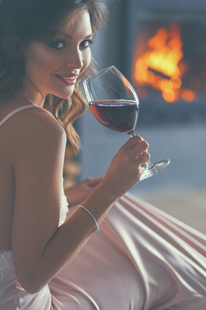 Woman with a glass of wine by the fireplace.の写真素材