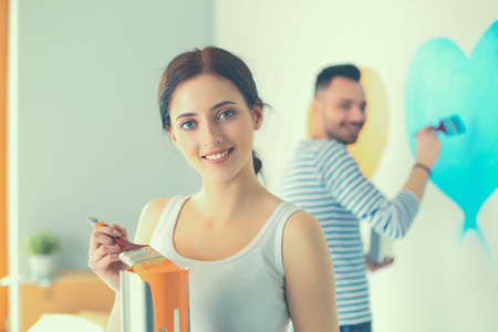 Portrait happy smiling young couple painting interior wall of new house.の写真素材