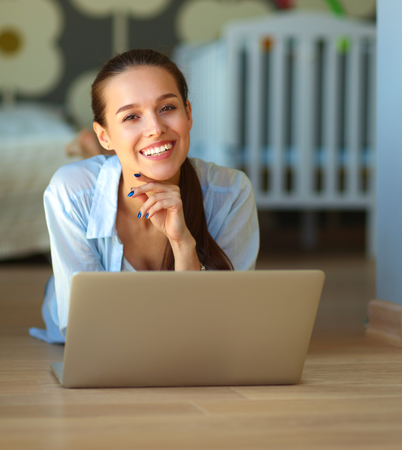 Young beautiful woman at home lying on the floor with laptopの写真素材