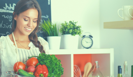 Smiling young woman holding vegetables standing in kitchenの写真素材