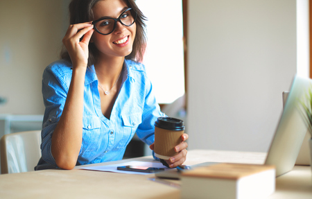 Young woman sitting in office table, looking at laptop computer screenの写真素材
