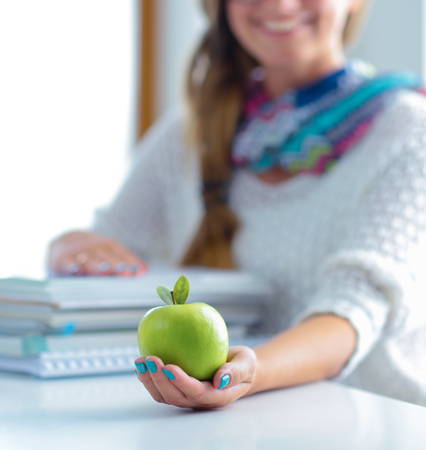 Female college students sitting on the desk with apple a pile of booksの写真素材