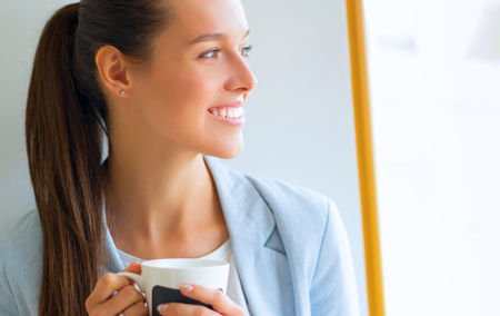 Attractive woman sitting at desk in office, working with laptop , having takeaway coffeeの写真素材