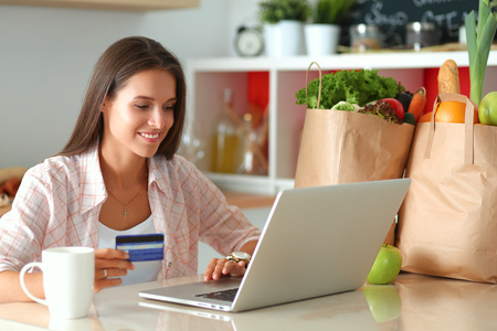 Smiling woman online shopping using tablet and credit card in kitchenの写真素材