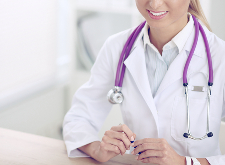 Beautiful young smiling female doctor sitting at the desk and writing.の写真素材