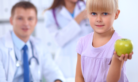 Child and medicine concept - female doctor giving an apple to little girlの写真素材
