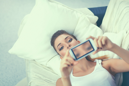 Happy brunette taking a photo of herself with her mobile phone in bedroomの写真素材