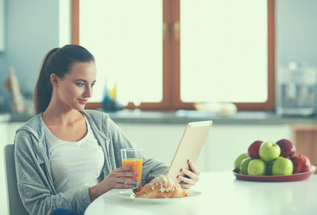 Young woman with orange juice and tablet in kitchenの写真素材