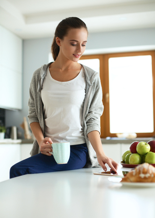 Happy woman drinking tea in the kitchen at homeの写真素材