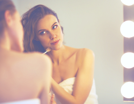 Young woman looking in the mirror and putting make-up onの写真素材