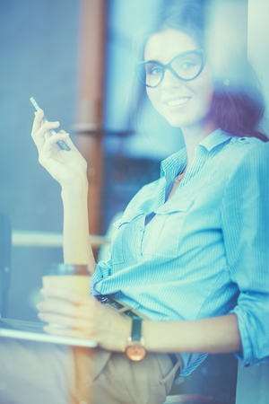 Young woman sitting at office table with laptop, view through windowの写真素材